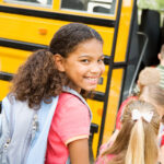 Little girl smiling while standing in line to get on school bus